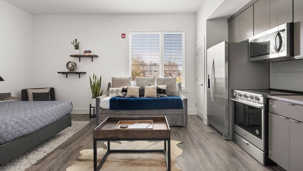 A modern kitchen with stainless steel appliances, a dining area with a wooden table, and a cozy seating area with a sofa and cushions.