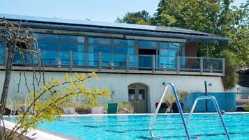 Una piscina con escalera metálica, una sala de yoga y un edificio con ventanas amplias y una puerta que indica “YOGA”.