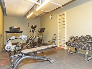 A gym with exercise equipment, a bench, dumbbells, and a clock on the wall.