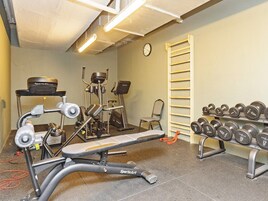 A gym with exercise equipment, a bench, dumbbells, and a clock on the wall.