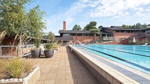 Ein Schwimmbecken mit einer gefliesten Liegefläche, umgeben von Blumentöpfen und einem Backsteinhaus im Hintergrund.