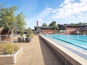 En swimmingpool med ett kaklat poolområde, omgiven av planterade blommor och en byggnad i tegel som syns i bakgrunden.