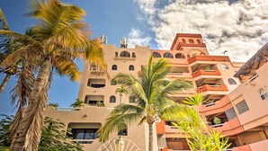 A multi-story hotel with balconies, palm trees, and a clear sky.