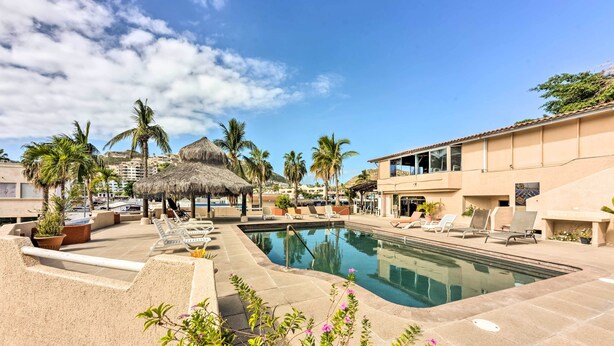 A pool area with lounge chairs, palm trees, and a building with a tiled roof.
