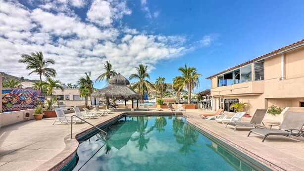 Une piscine avec des chaises longues, des palmiers et un bâtiment doté d’un toit en tuiles.