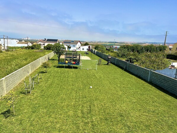 Un jardin arrière bien entretenu, avec une pelouse, une balançoire, un petit espace de jeux et une clôture périphérique.