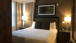 Quarto de hotel com uma cama grande, duas mesas de cabeceira com luminárias, um ventilador de teto e um quadro na parede.