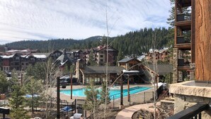 Um resort com piscina, área de estar externa e vista para os edifícios e montanhas ao redor.