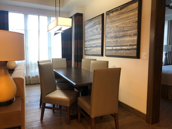 A dining area with a dark wooden table and six chairs, two large abstract paintings on the wall, and a modern pendant light.