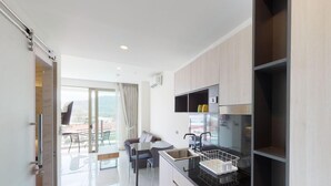 A modern kitchen with a dining area, a sliding glass door leading to a balcony, and a view of the cityscape. - Oceana C51 (Kamala)
