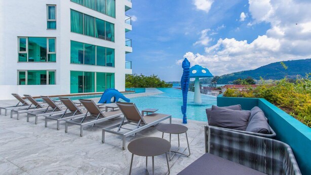 A poolside area with lounge chairs, a blue seahorse sculpture, and a view of a mountain range. - Oceana C51 (Kamala)