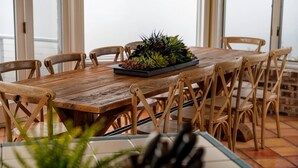 Une table à manger en bois, avec des chaises, un arrangement floral en guise de centre de table et un sol carrelé.