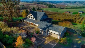 Une grande maison avec un garage, entourée d’un jardin aménagé et offrant une vue sur des collines ondulantes.