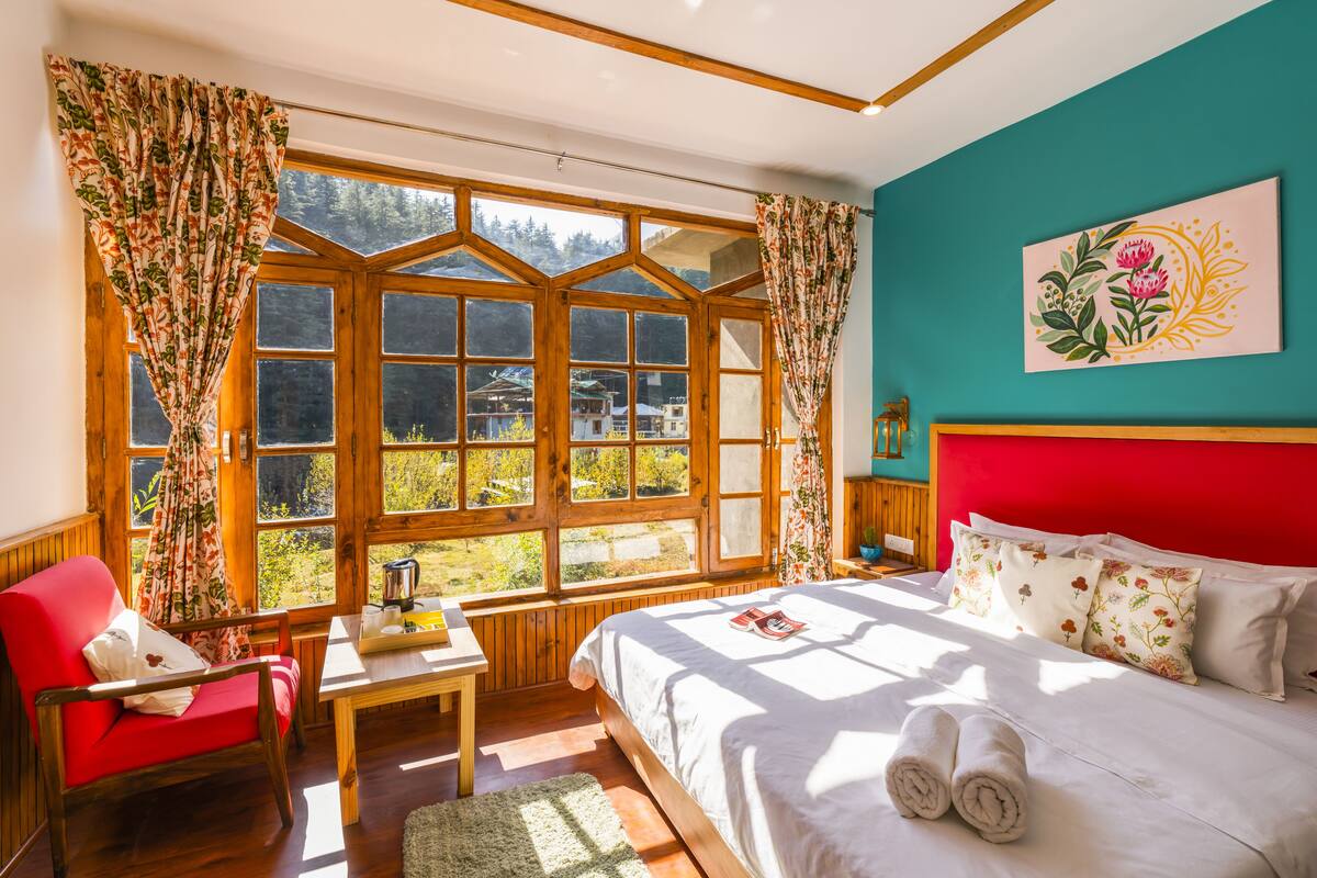 A bedroom with a large window, wooden furniture, a red headboard, and a floral painting on the wall.