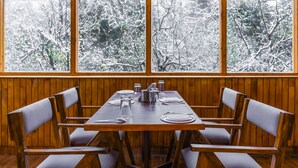 Un coin repas avec une table en bois dressée pour quatre personnes, entourée de chaises, et de grandes fenêtres donnant sur des arbres couverts de neige.