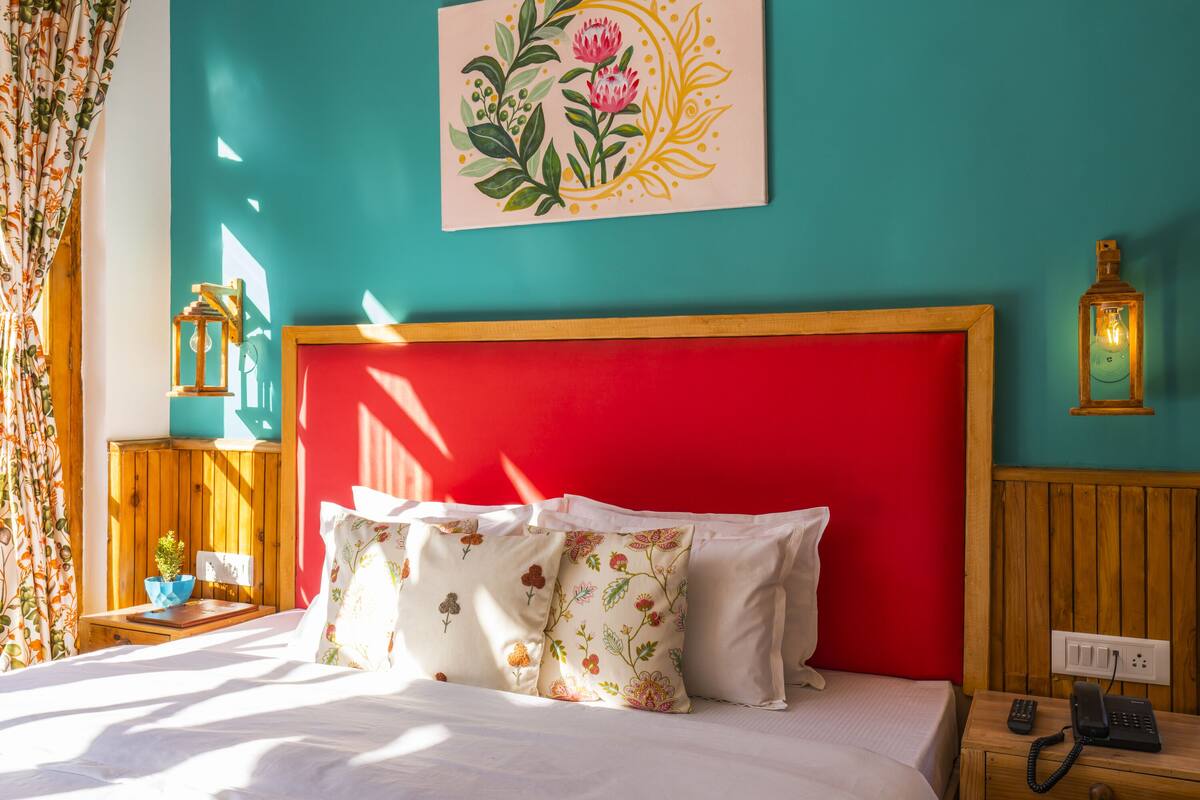 A bed with floral pillows, a red headboard, and a wall-mounted artwork.