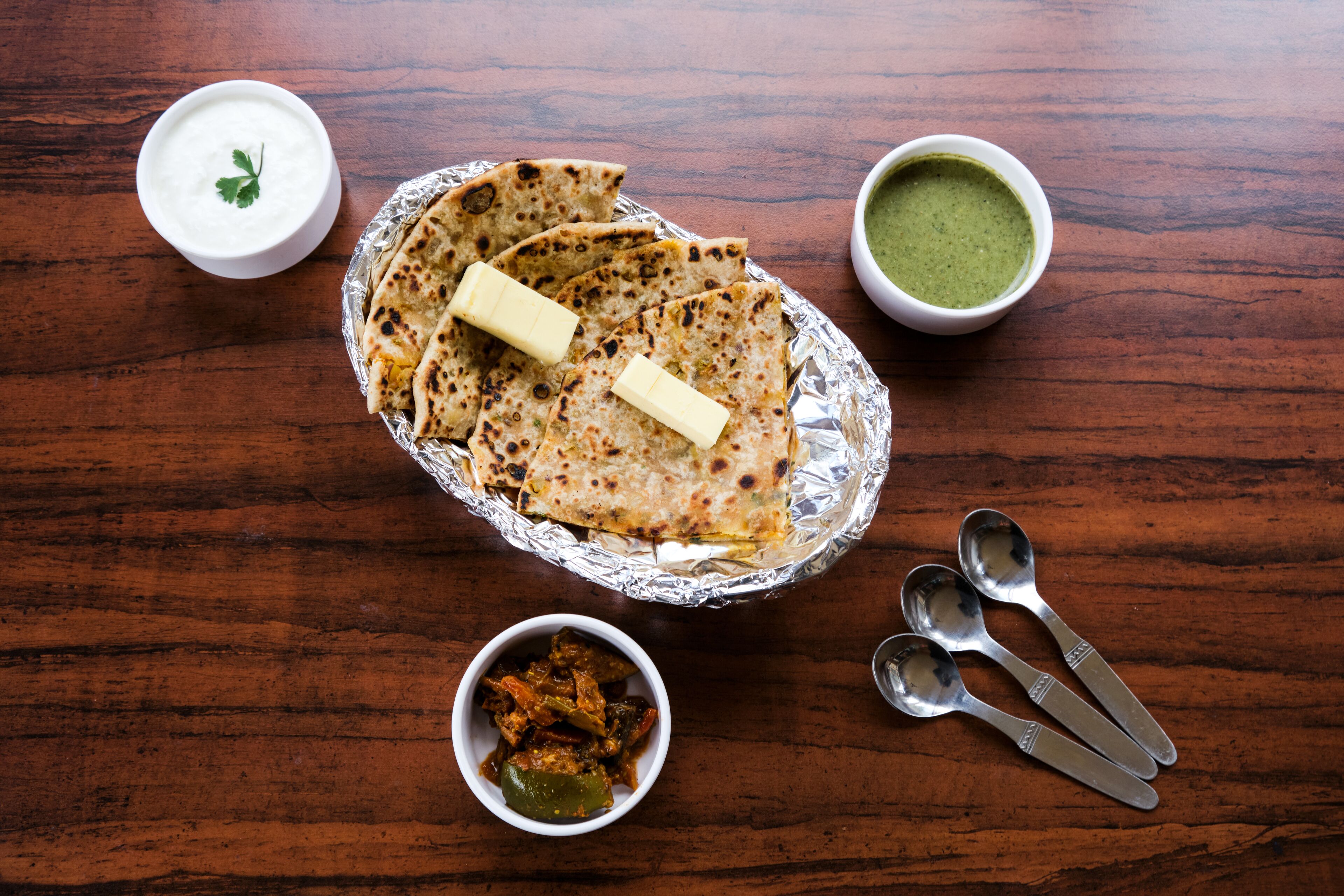A meal with flatbread, butter, and two types of sauces on a wooden table.