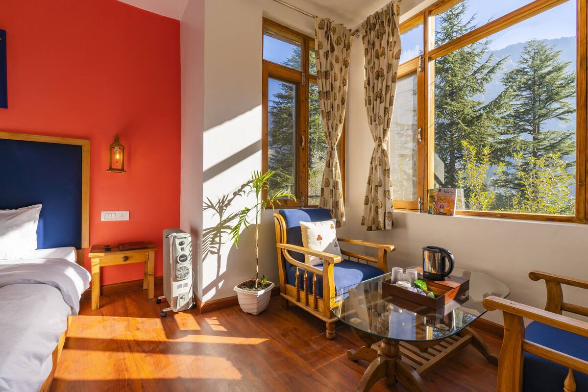 A room with a bed, a chair, a table, a heater, a potted plant, and a window with curtains.