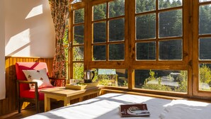 Une pièce chaleureuse avec un lit en bois, une chaise rouge, une petite table et une fenêtre donnant sur des arbres.