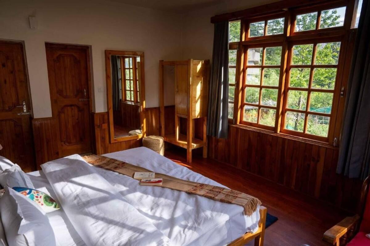 A wooden-paneled room with a large bed, a wooden wardrobe, and a window with a view of greenery.