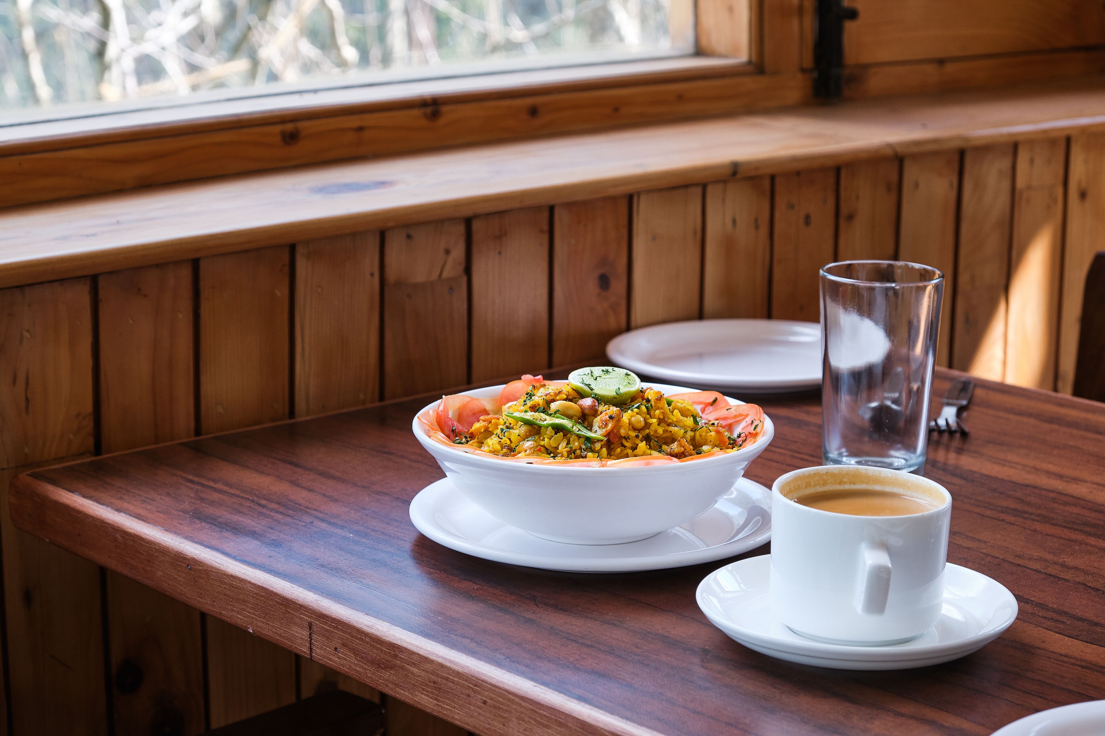Una mesa de madera con un bol de comida, un vaso de agua y una taza de café.