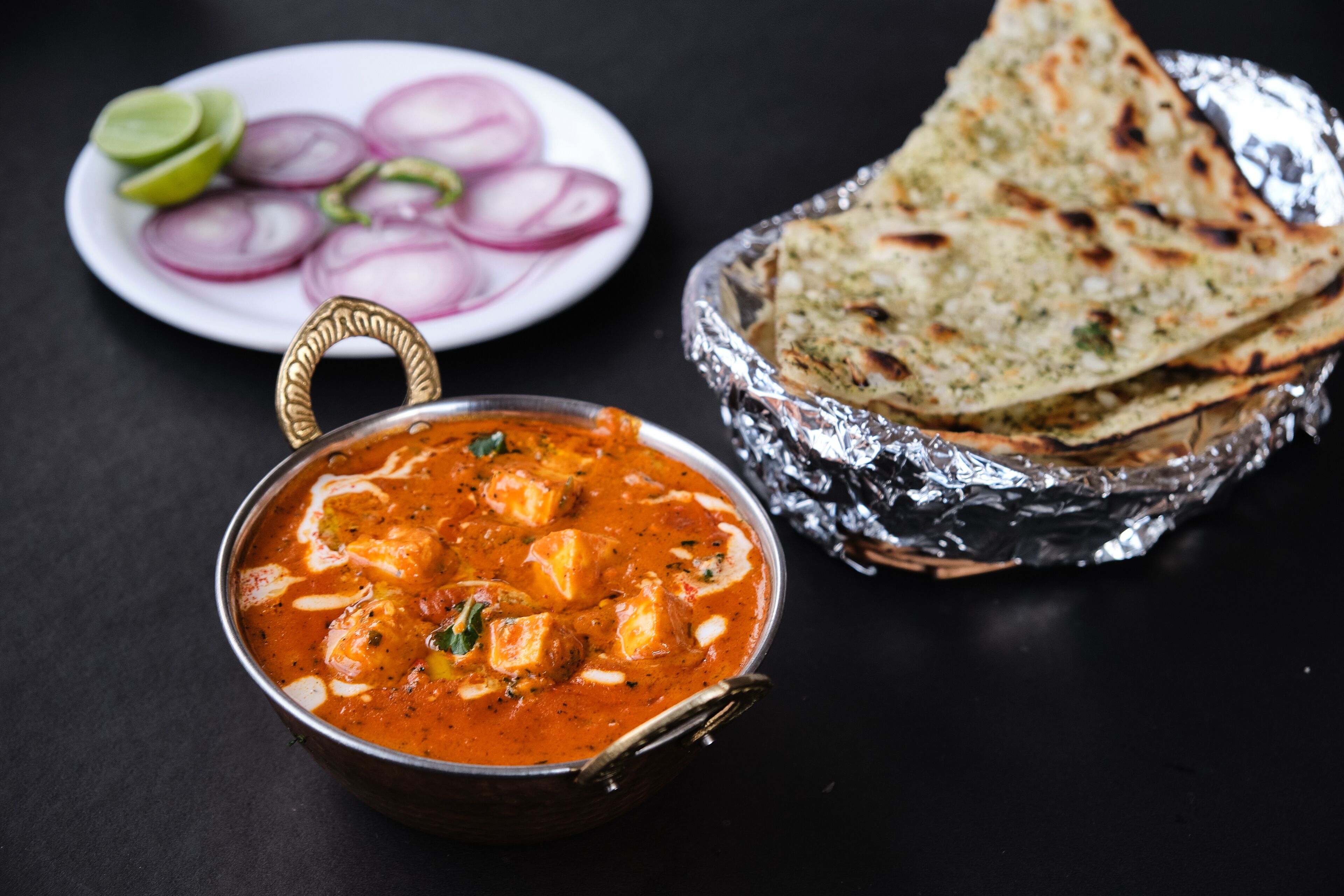 Un bol de paneer tikka masala, accompagné de pain naan et d’oignons coupés en tranches.