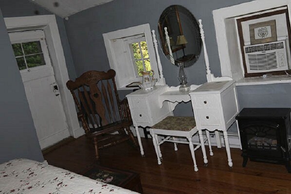 A room with a wooden chair, a white dresser, a mirror, and a small table.