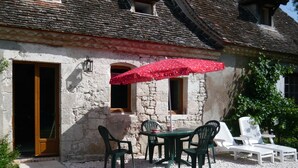 A stone building with a tiled roof, a wooden door, and a small window. There is a table with chairs and a red umbrella. - Luxury gite for adult couples, peaceful, open views, large swimming pool (Boisse)