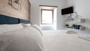 A modern bedroom with a wooden headboard, a large bed, a mounted TV, a bicycle, and a window with a view. - Italianway - Roma 38 (Bormio)