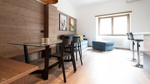 A modern living room with a glass dining table, dark chairs, a blue sofa, and a large window. - Italianway - Roma 38 (Bormio)