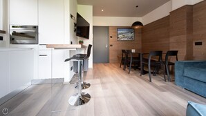 A modern kitchen with built-in appliances, a dining area with a wooden wall and a painting, and a blue sofa in a living space. - Italianway - Roma 38 (Bormio)