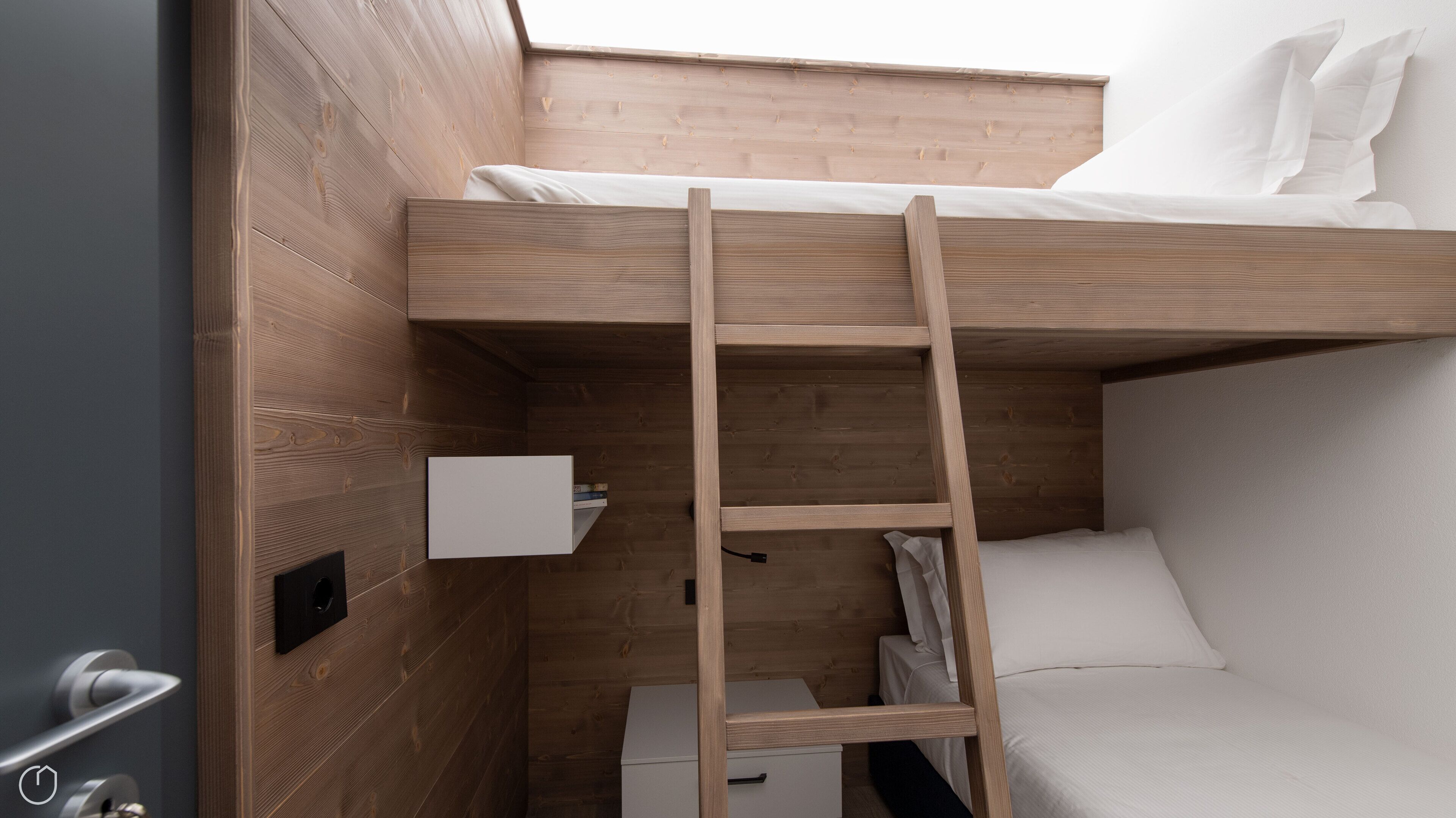 Un lit superposé avec une échelle en bois, une table de chevet et une petite armoire blanche.