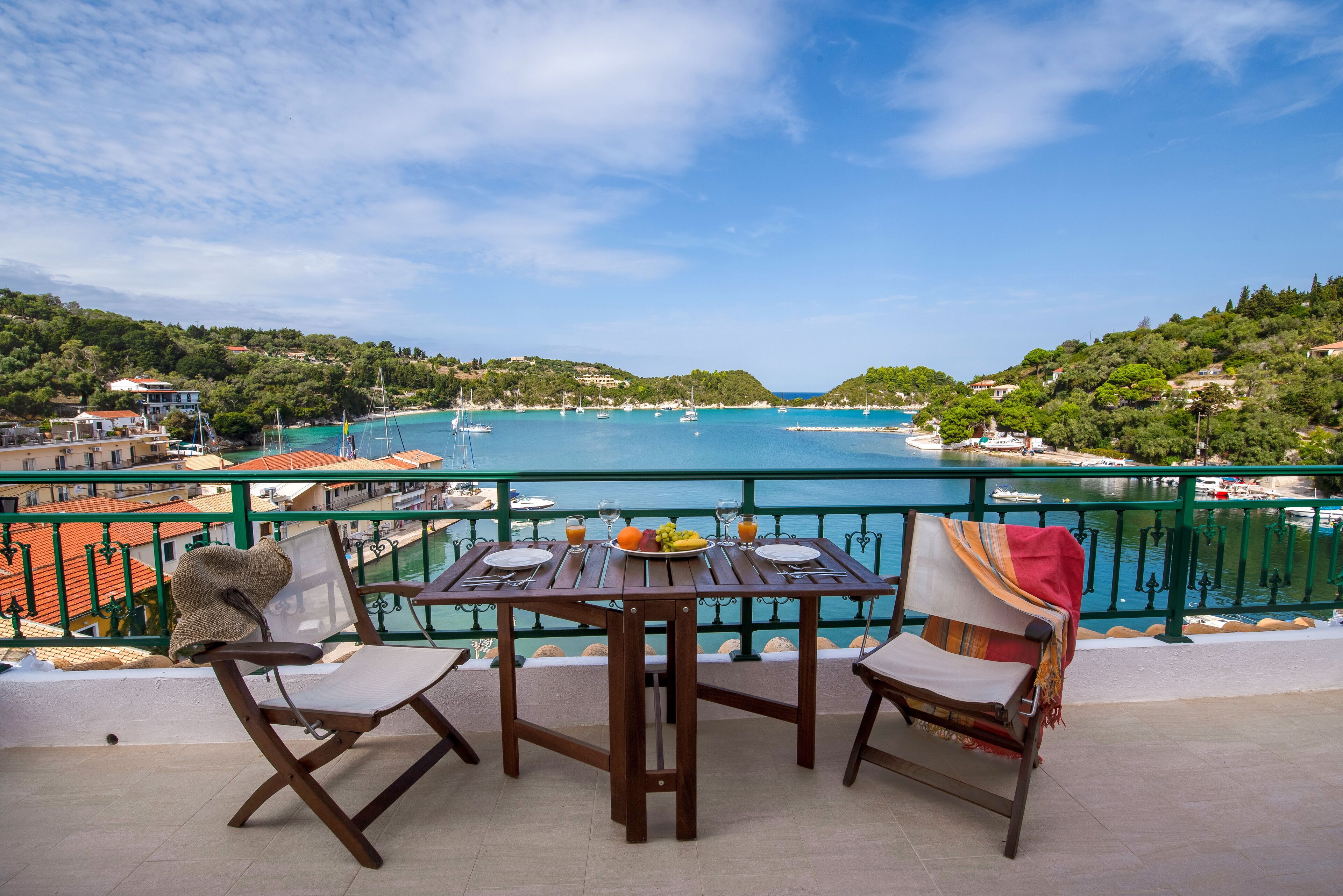A terrace with a table set for two, overlooking a coastal area with boats and a clear sky.