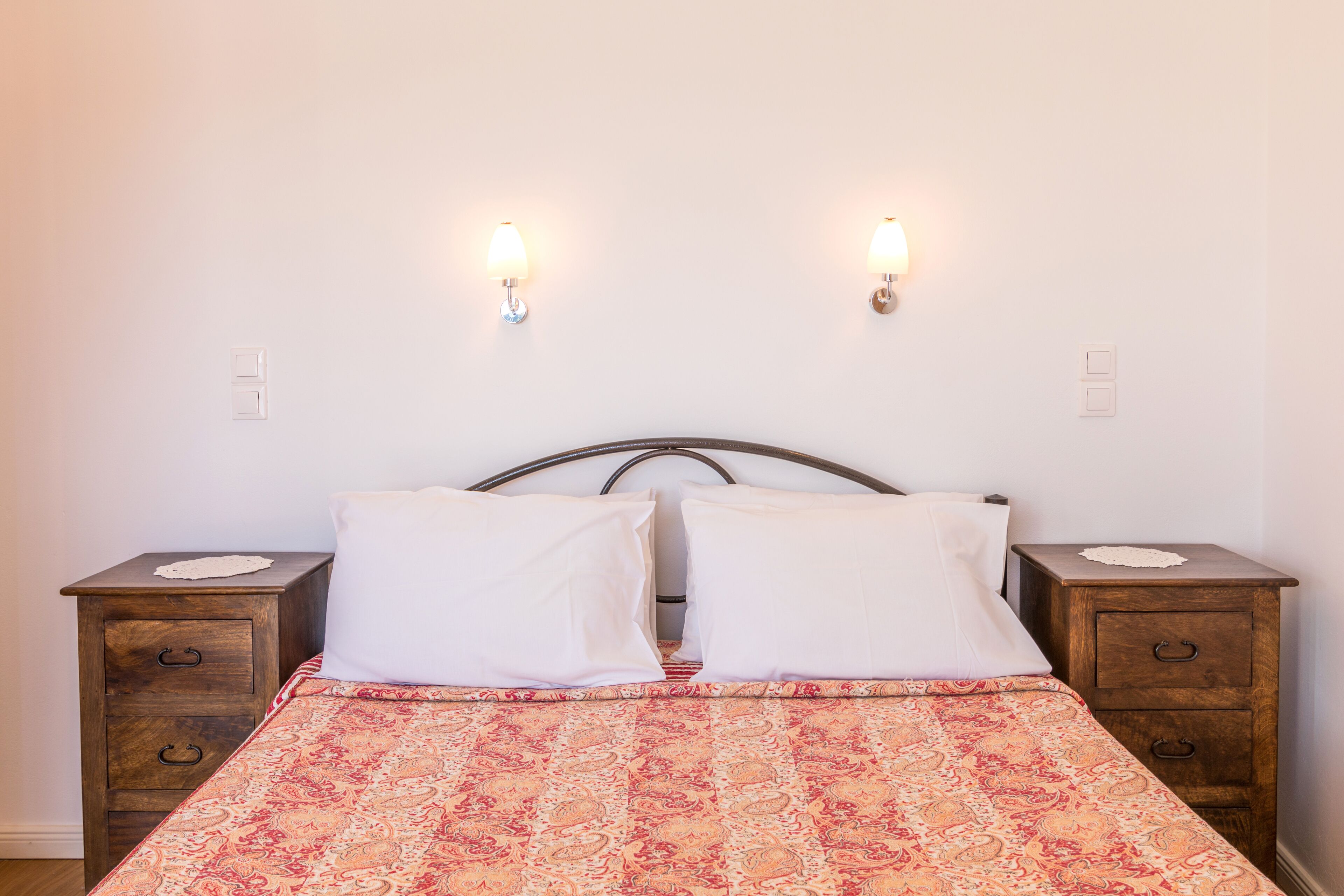 Un letto con copriletto decorato, due comodini e lampade a parete.