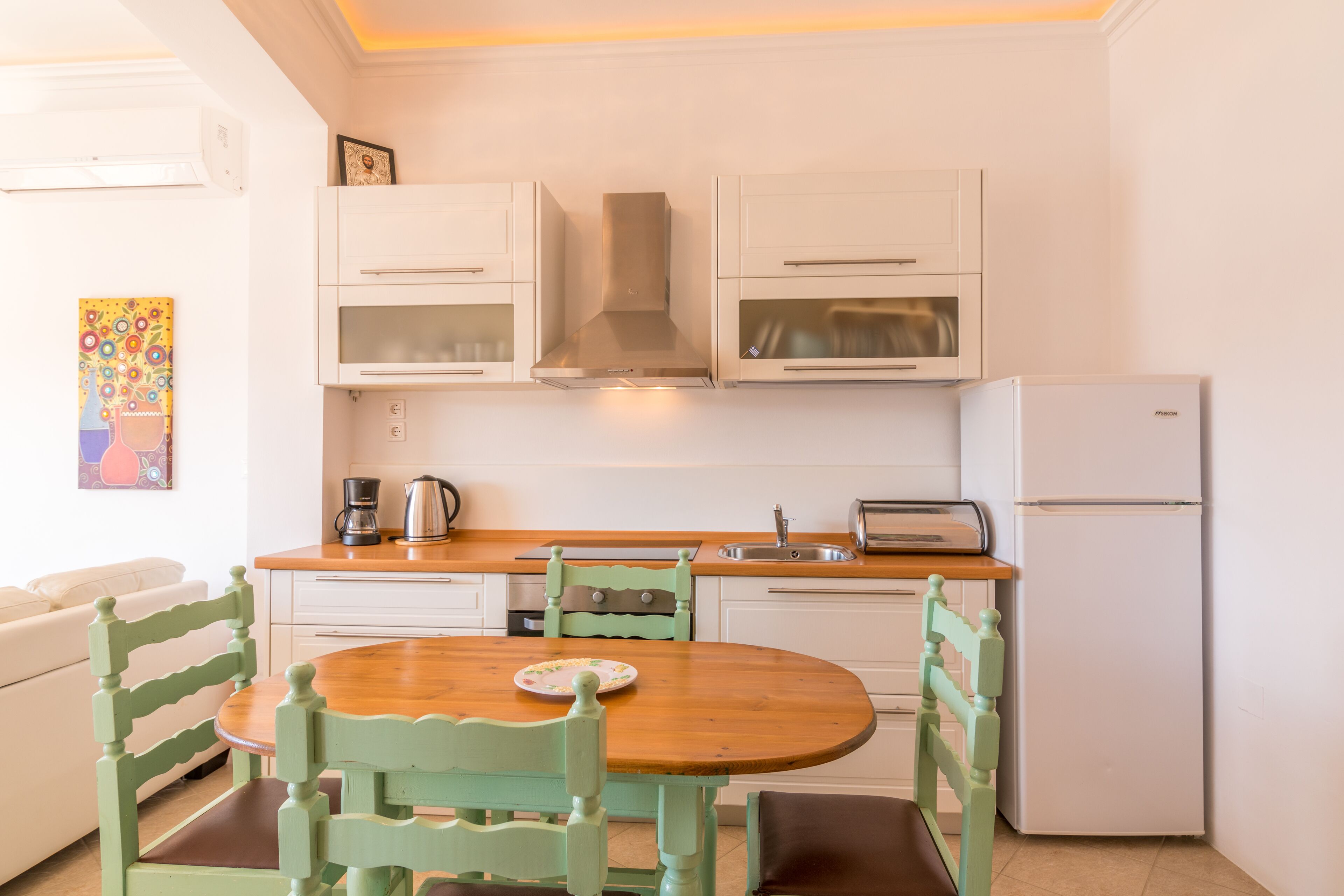 Une cuisine de taille réduite avec des meubles blancs, une table en bois et des chaises assorties.