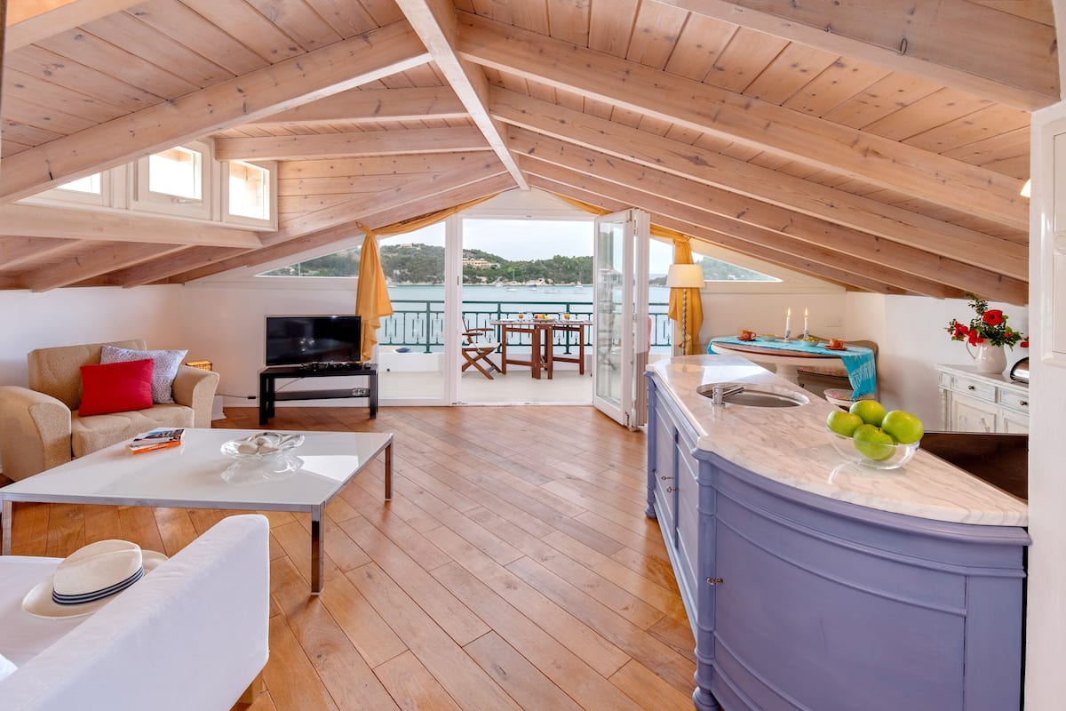 Un loft spacieux avec un plafond en bois, un coin repas offrant une vue sur la mer et une cuisine dotée d’un plan de travail en marbre.
