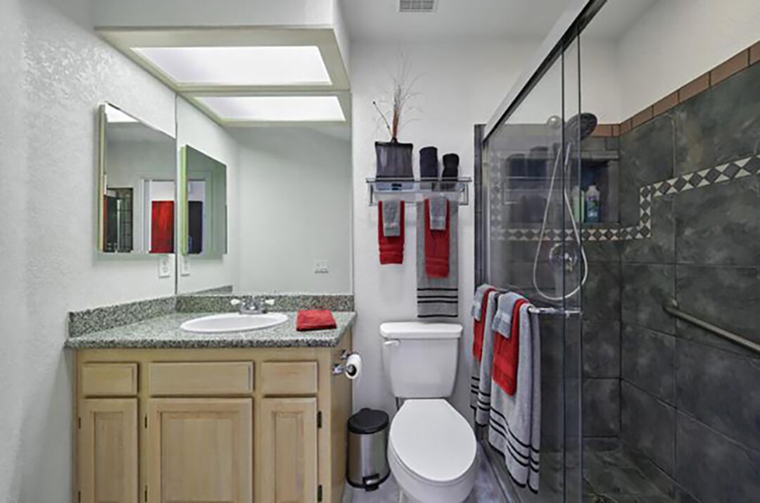 A bathroom with a granite countertop sink, a toilet, a glass shower enclosure, and a mirror above the sink.