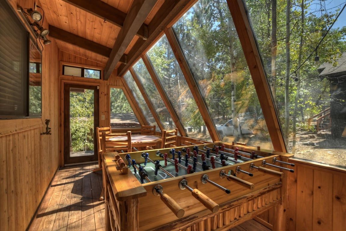 A wooden interior with a foosball table, large windows, and a view of the outdoors.