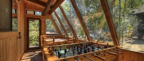 A wooden interior with a foosball table, large windows, and a view of the outdoors.