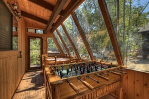 Un intérieur en bois agrémenté d’un baby-foot, de grandes fenêtres et d’une vue sur l’extérieur.