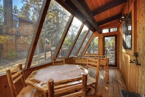 Un intérieur en bois avec une table ronde et des chaises, un baby-foot et de grandes fenêtres donnant sur l’extérieur.