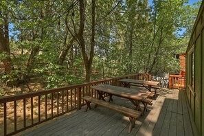 A wooden deck with picnic tables, surrounded by trees. - Peace Out by Destination Big Bear : Remarkable Dutch Gambrel Only 2 Blocks from Snow Summit! Foosball! (Big Bear Lake)