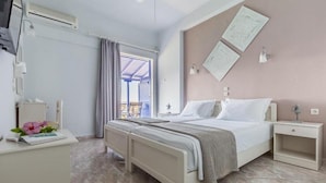 A hotel room with a bed, bedside tables, a desk with a chair, an air conditioning unit, and a window with curtains. - Oniro Pension (Alonissos)