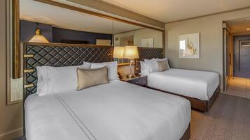 A hotel room with two beds, a large mirror, a bedside table with a lamp, and a framed picture on the wall.