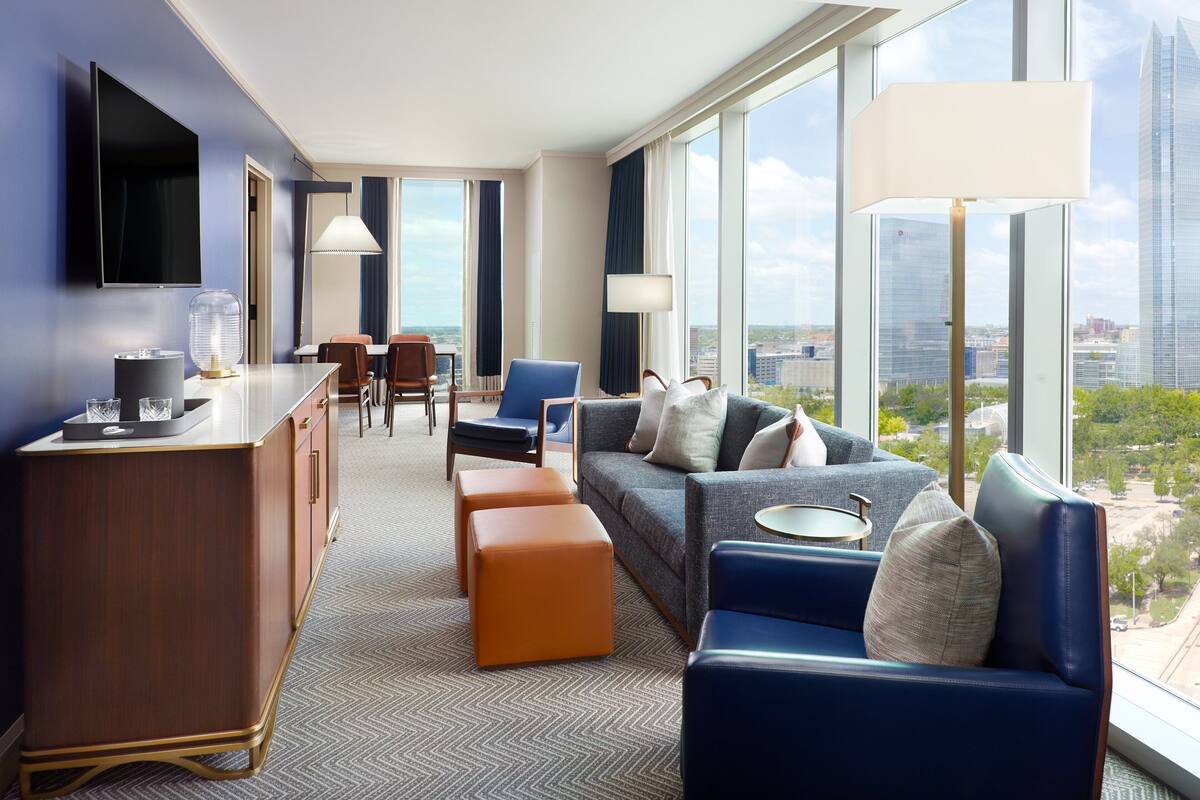 A modern hotel room with a dining area, a sofa set, and a city view.