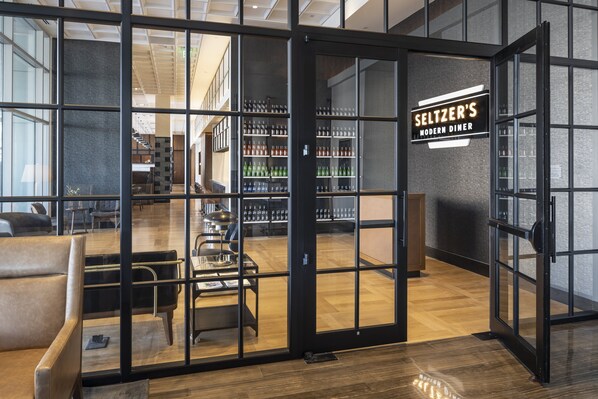 Interior moderno de una cafetería con puerta de cristal, zona de mesas y barra visible.
