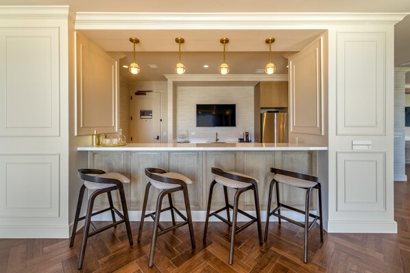 A kitchen with a central island, bar stools, pendant lighting, and a stainless steel refrigerator.
