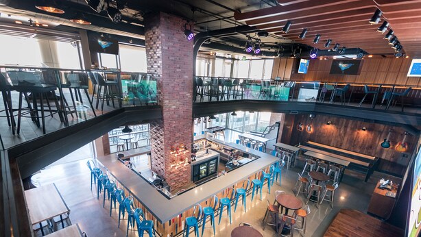 Un restaurante de varios niveles con una zona de bar central, arreglos de asientos y vistas del espacio interior.