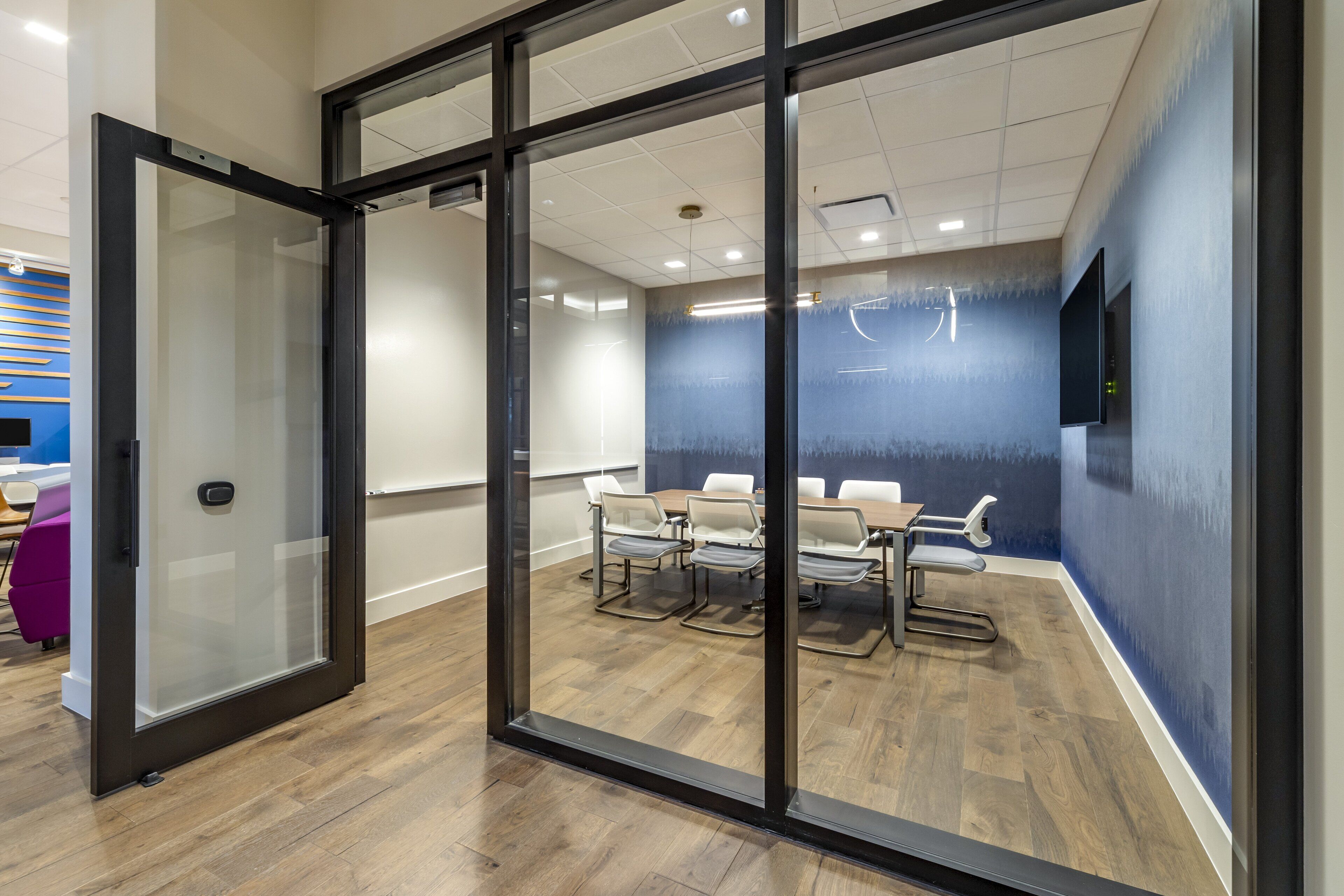 A modern conference room with glass walls, a wooden floor, and a blue accent wall.