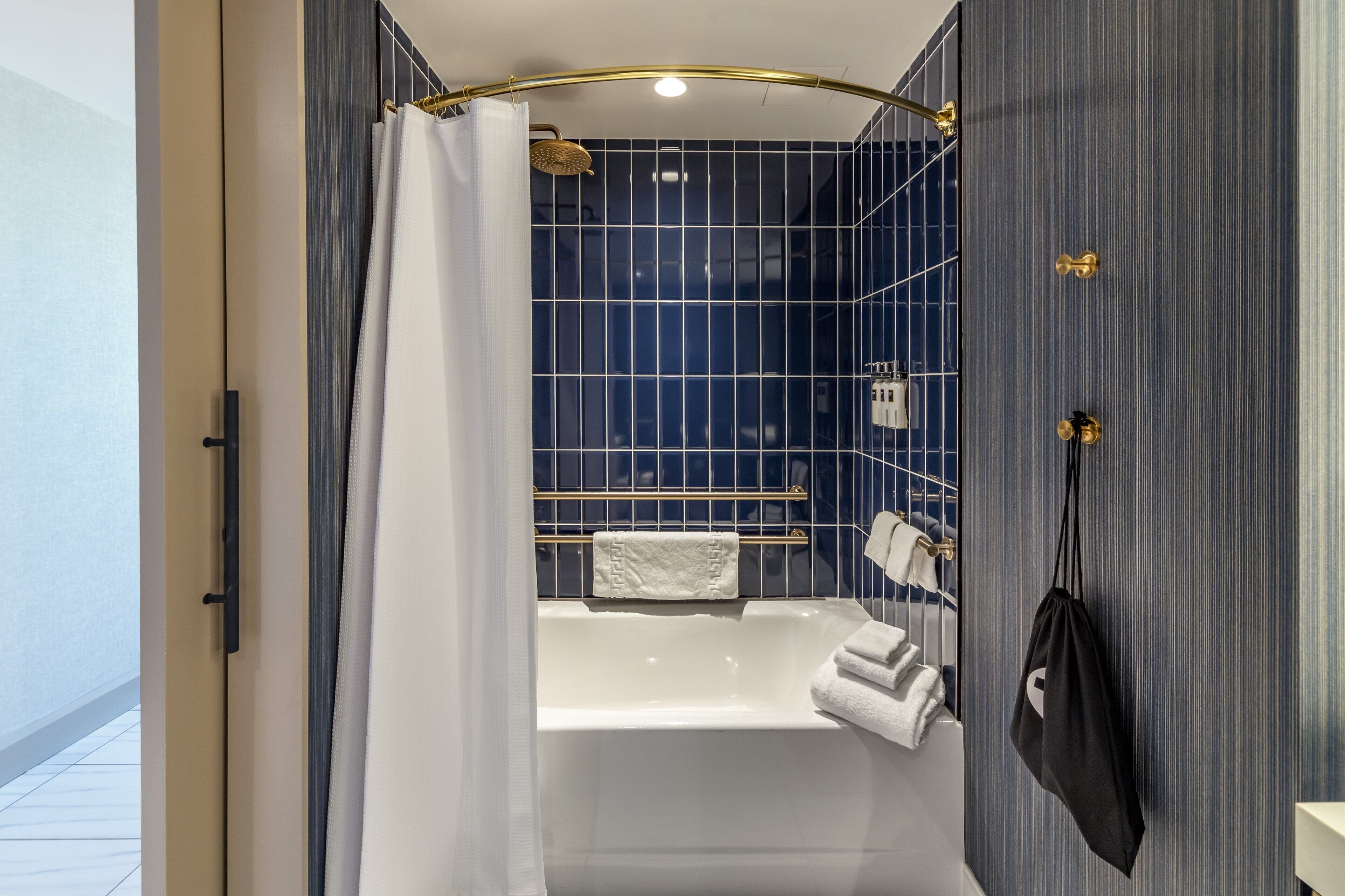 A modern bathroom with a bathtub, a shower with a gold shower head, and a towel rack with multiple towels.